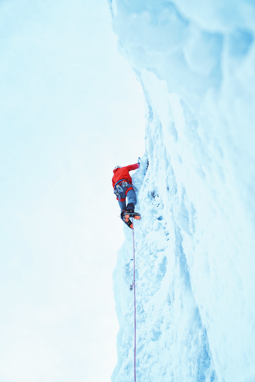 person wearing red jacket climbing on glacier