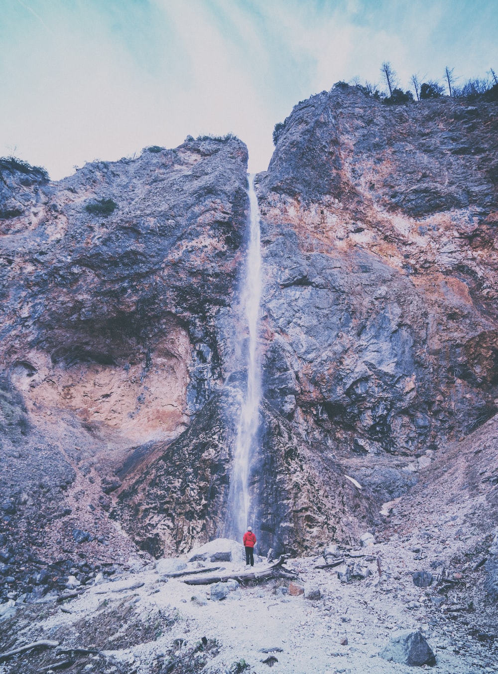 person wearing red jacket standing near waterfalls