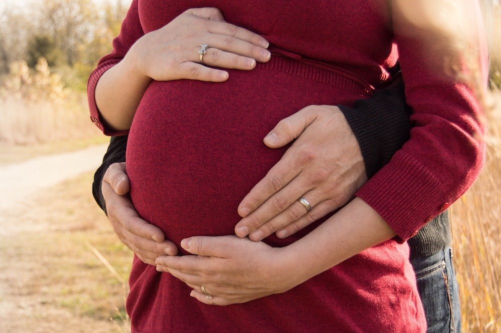 pregnant woman standing behind the man holding tummy