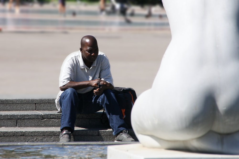 selective focus photography of man sitting beside water fountain with statue