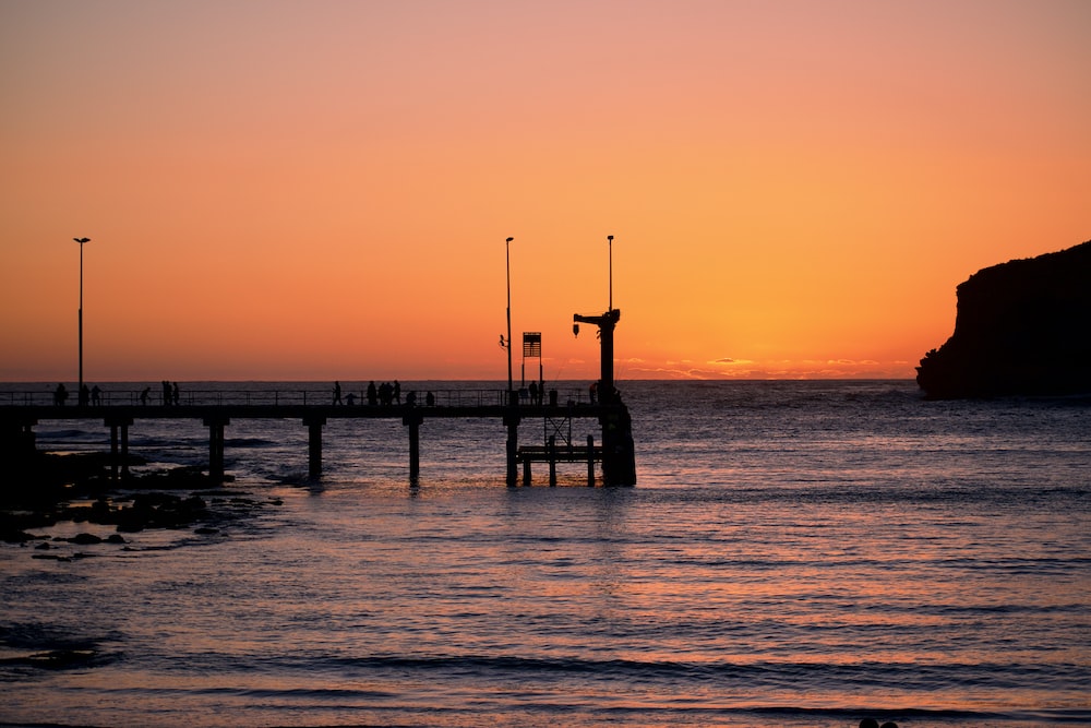 silhouette of dock beside sea during golden houer
