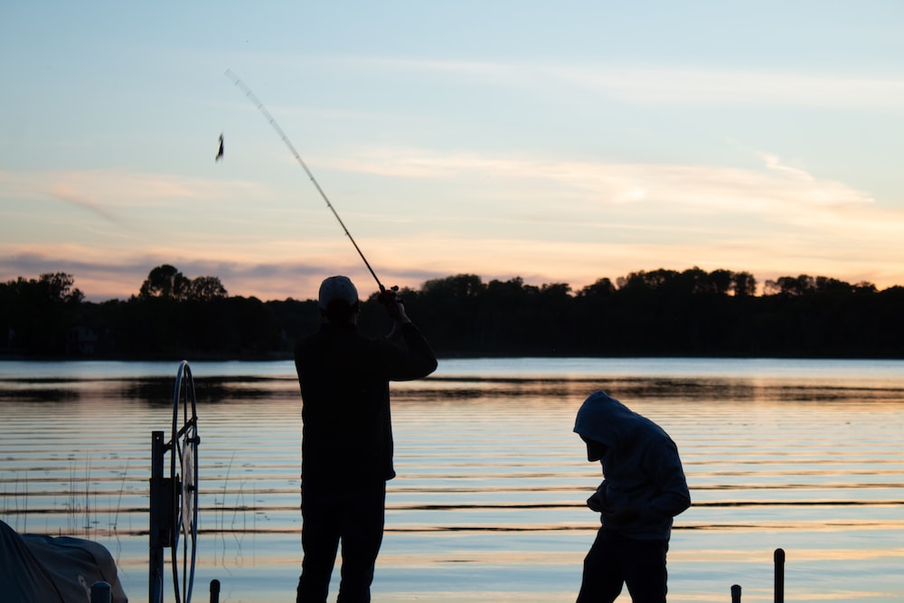 two men fishing on a lake at sunset