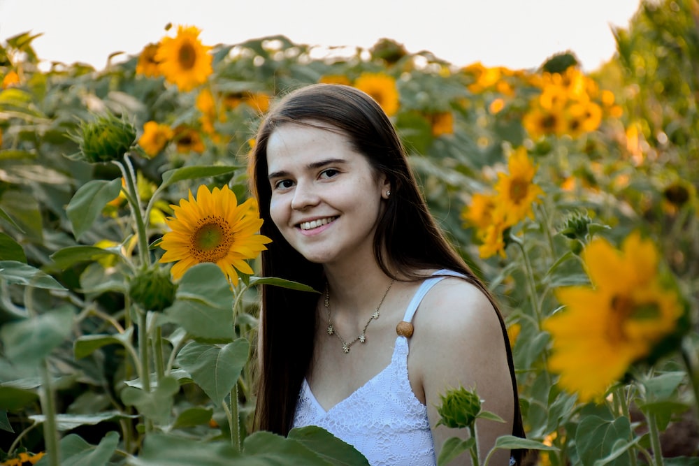 woman in white tank top standing on sunflower field during daytime