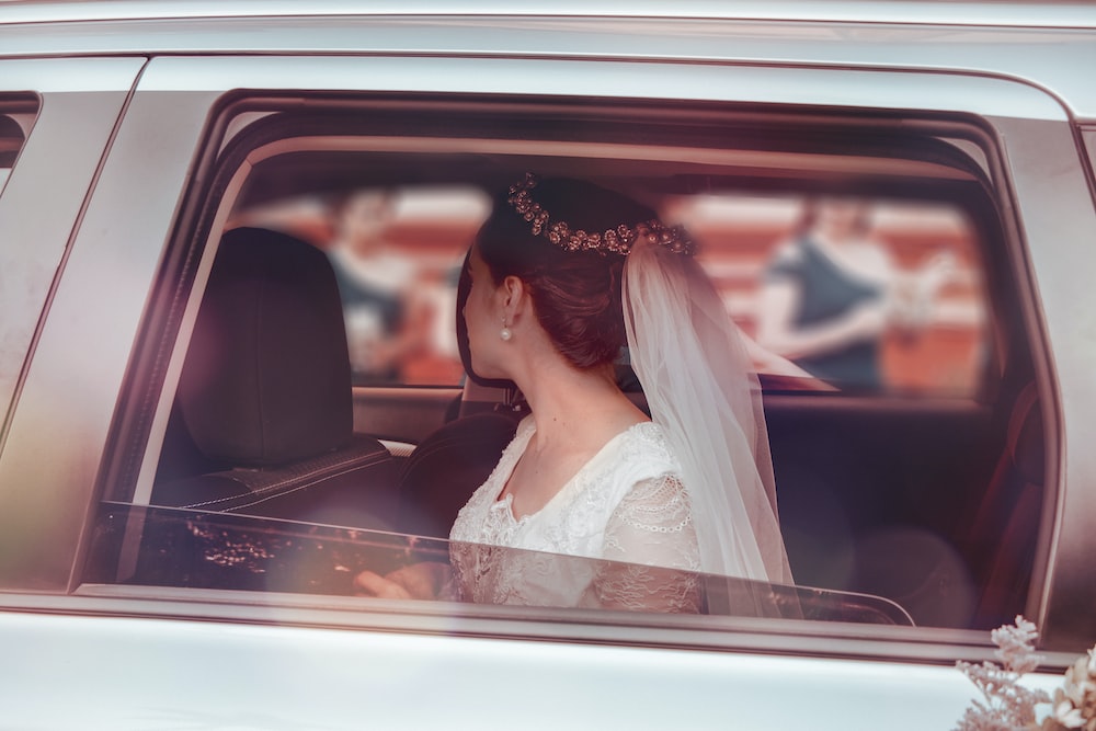 woman in white wedding gown sitting on car seat
