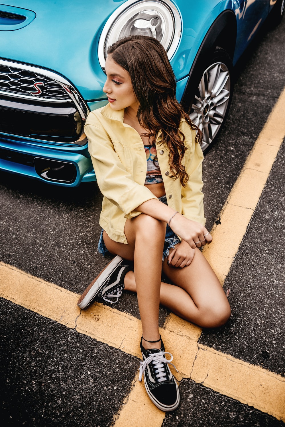 woman wearing yellow button-up jacket sitting besides blue car